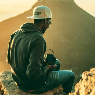 a photographer with a backwards cap sitting on a rock